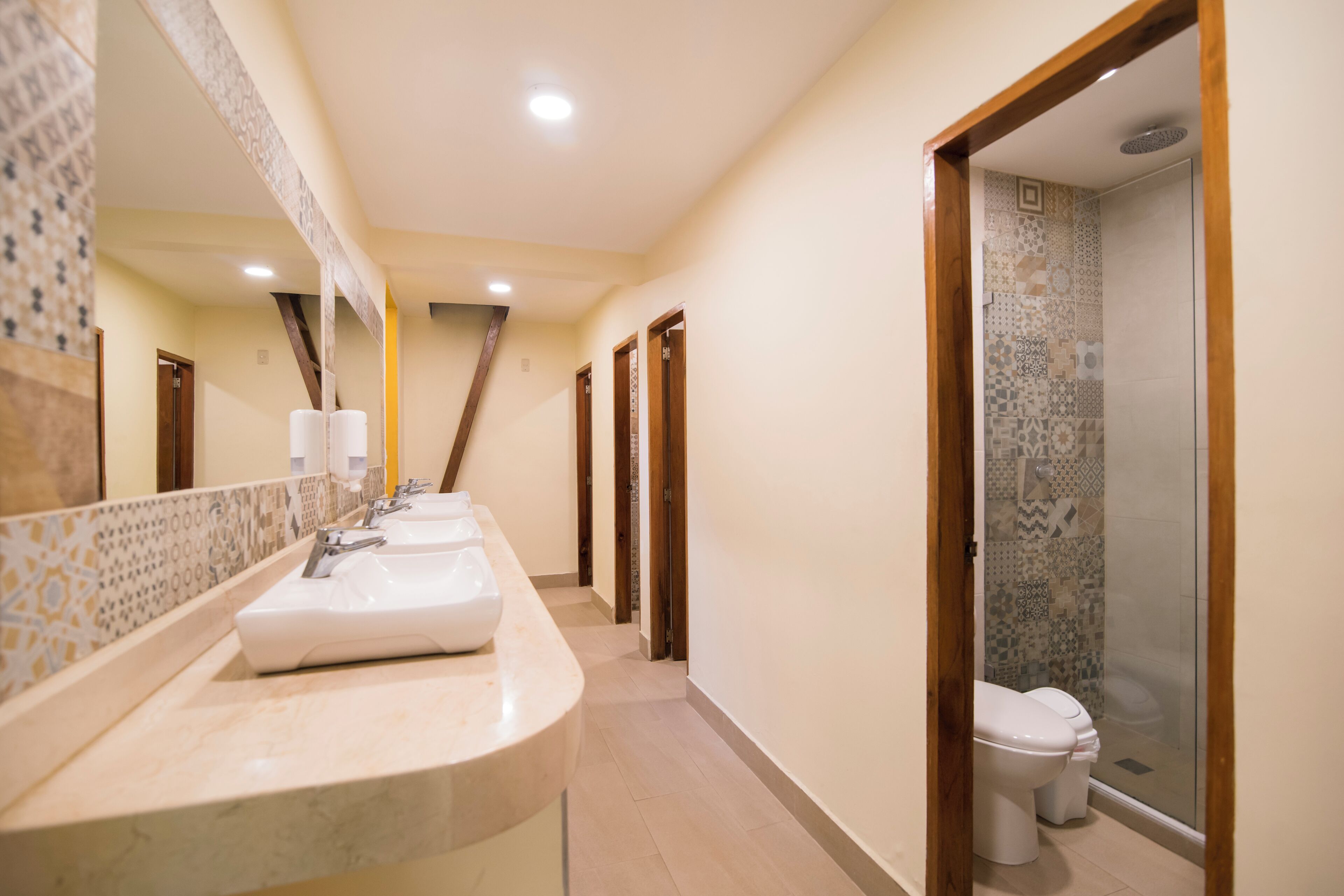 A hotel bathroom with a long vanity, multiple sinks, a large mirror, and a shower area.