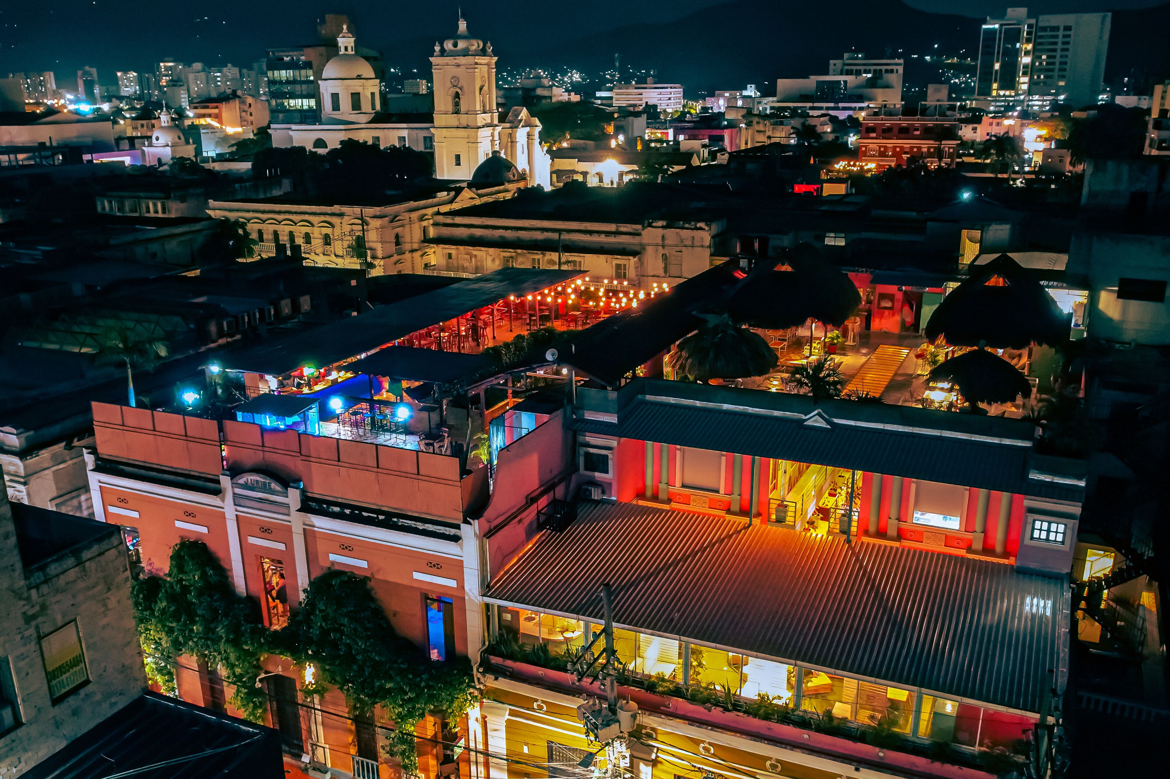 A hotel with a rooftop terrace, a dining area with outdoor seating, and a view of the cityscape at night.