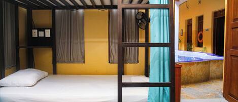 Une chambre avec un lit superposé en bois, une petite étagère avec quelques objets et une fenêtre avec des rideaux.