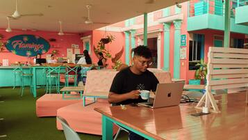 Une pièce lumineuse aux murs turquoise et rose, dotée d’un ventilateur de plafond et d’une enseigne sur laquelle on peut lire « Flamingo ».
