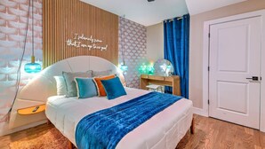 Quarto moderno com cama, mesa de cabeceira e parede com uma frase motivacional.