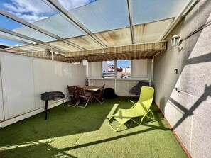 Una terraza en la azotea con una mesa y sillas, una silla amarillo brillante, y una vista a través de una ventana.