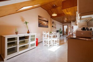 A spacious kitchen with wooden beams, a dining area with white chairs, and a tiled floor. - Natural Light (Madrid)