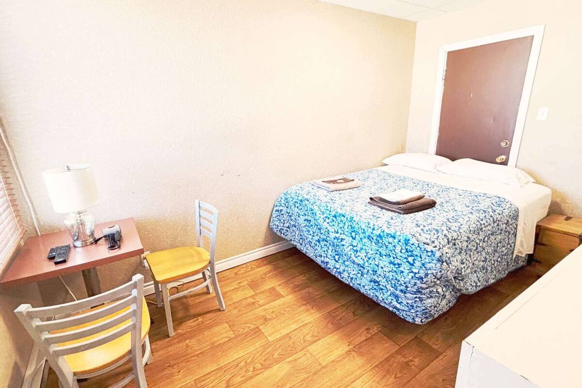 Una habitación pequeña con cama, escritorio, silla y ventana con persianas.