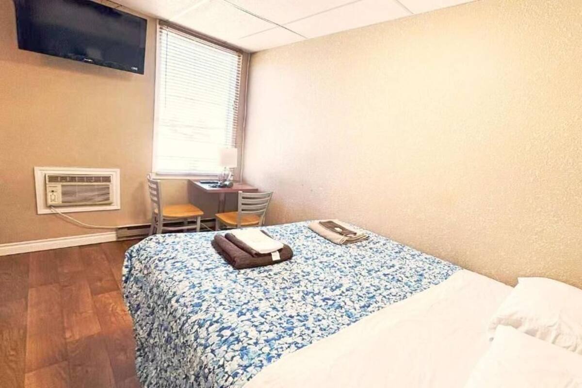 Habitación de hotel con cama, escritorio, silla, televisor montado en la pared y ventana con persianas.