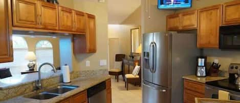 Una cocina con armarios de madera, un refrigerador de acero inoxidable, un microondas y un televisor montado en la pared.