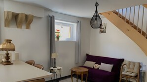 A modern living room with a dining area, a purple sofa, a wooden chair, a small table, and a staircase.