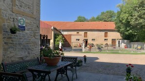 A courtyard with a stone wall, a bench, a table, and a building with a red roof in the background.