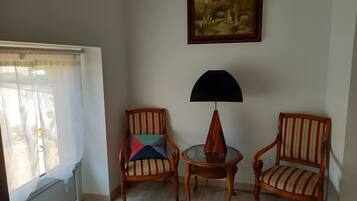 Una habitación con dos sillas de madera, una mesa con superficie de vidrio, una lámpara y un cuadro en la pared.