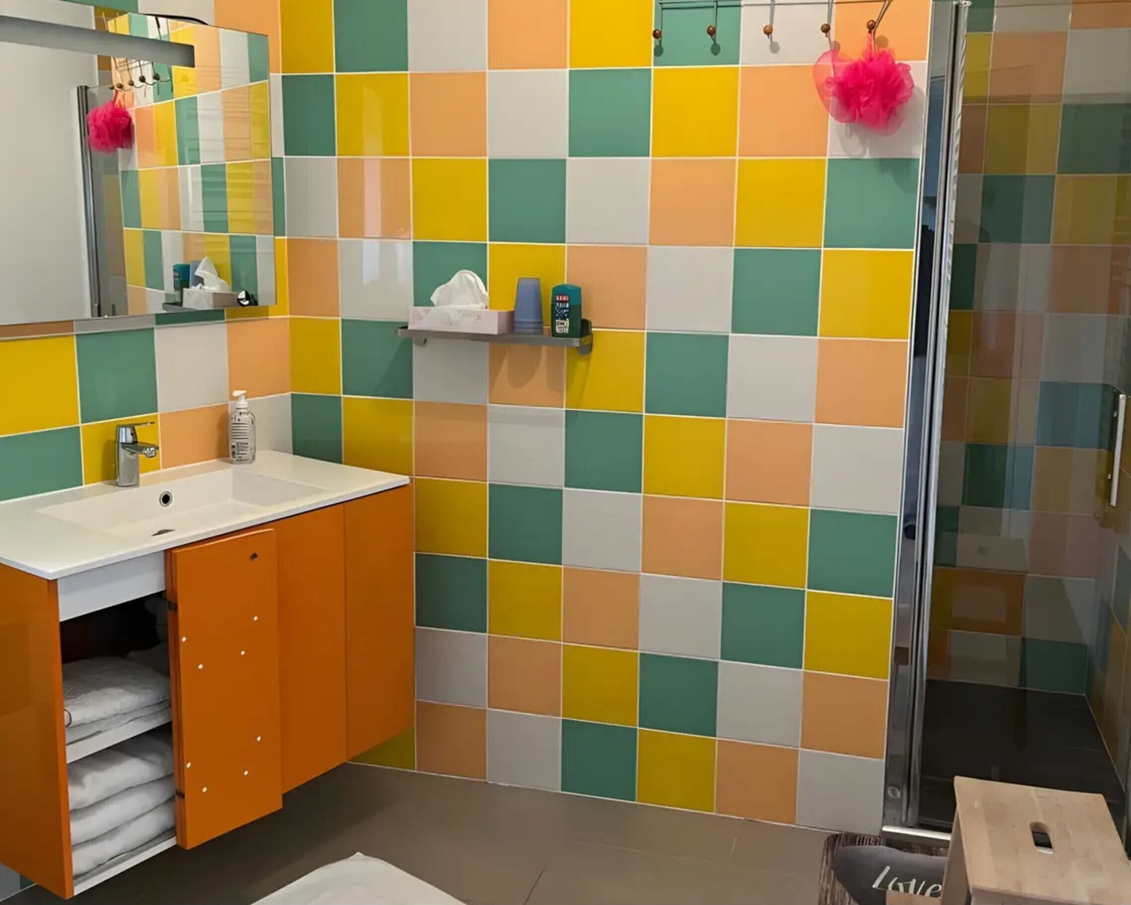 Een badkamer met een kleurrijke betegelde spatwand, een wastafel met spiegel en een douchehoek.