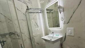 A modern bathroom with a glass-enclosed shower, a sink with a mirror above it, and a toilet. - LBC Hotel (Sarandë)