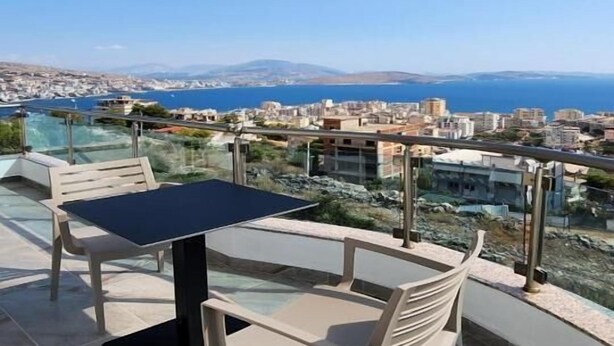 A balcony with a table and chairs overlooking a coastal cityscape. - LBC Hotel (Sarandë)