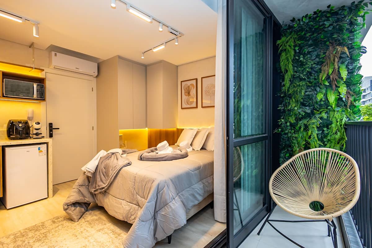 A modern bedroom with a bed, bedside table, and a small kitchenette.