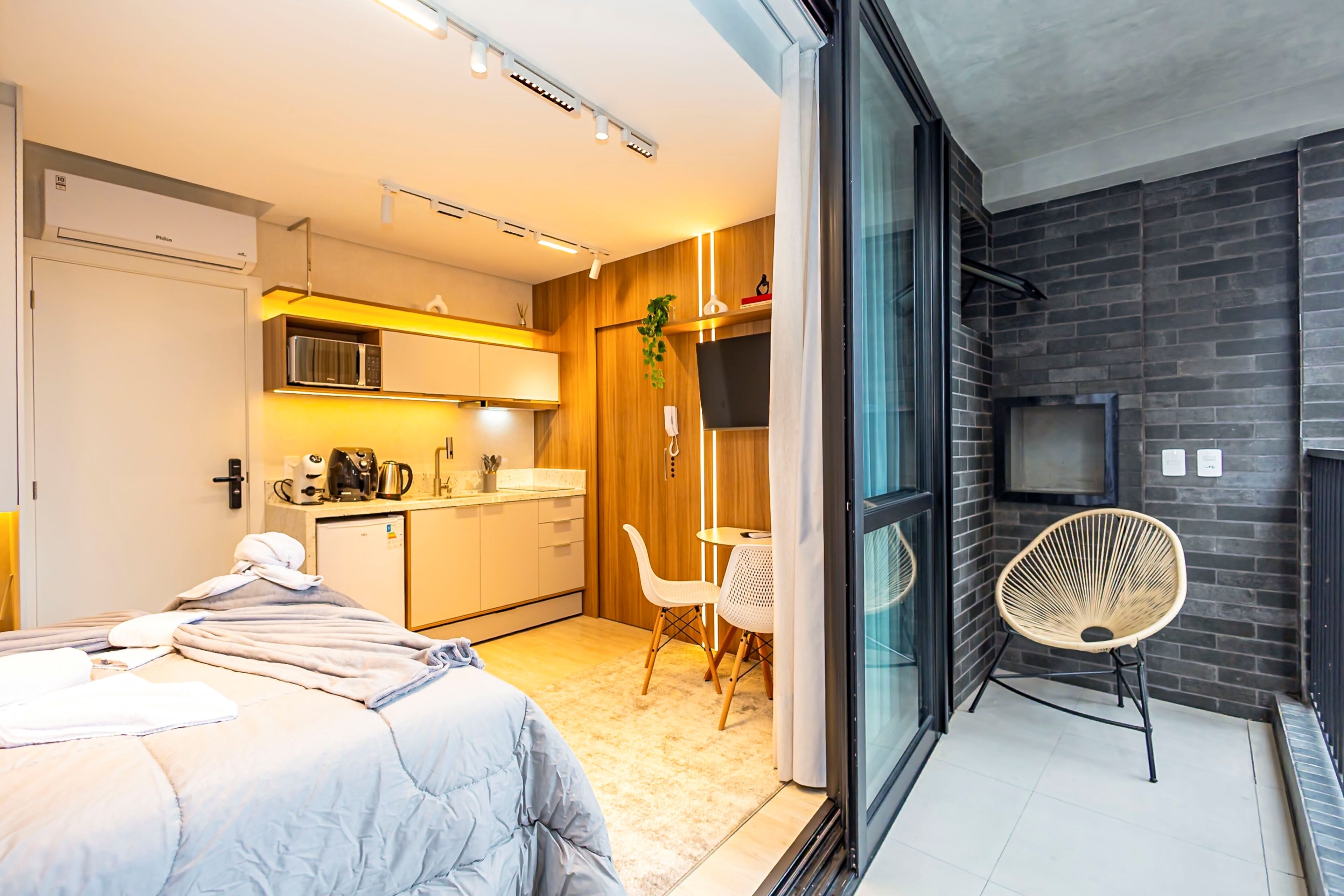 A modern hotel room with a bed, kitchenette, and a balcony with a chair.