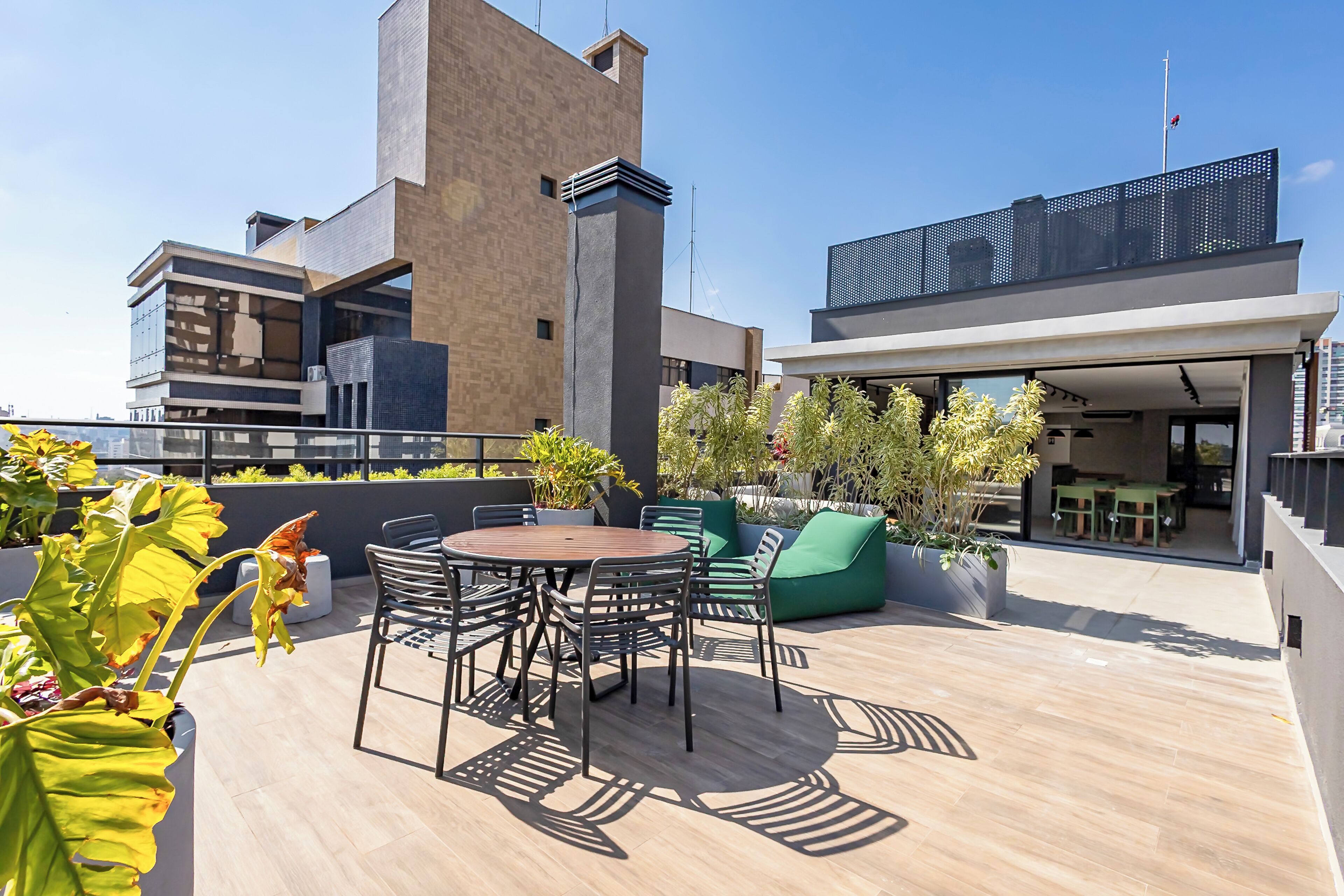 Una terraza en la azotea con una mesa redonda, sillas y asientos verdes.