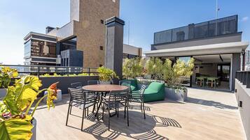 Una terraza en la azotea con una mesa redonda, sillas y asientos verdes.