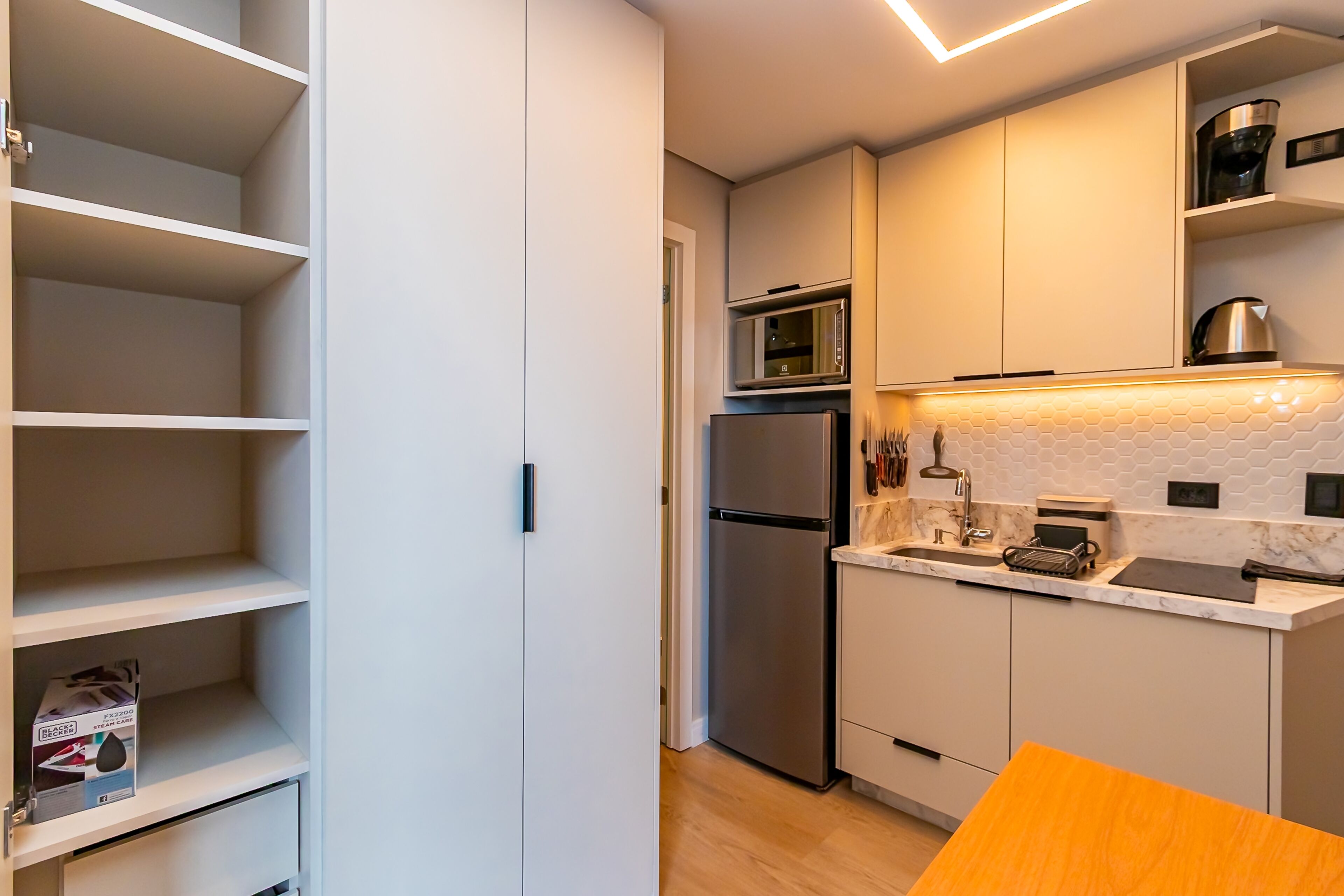 A modern kitchen with white cabinets, a stainless steel refrigerator, a microwave, and a sink with a tiled backsplash.