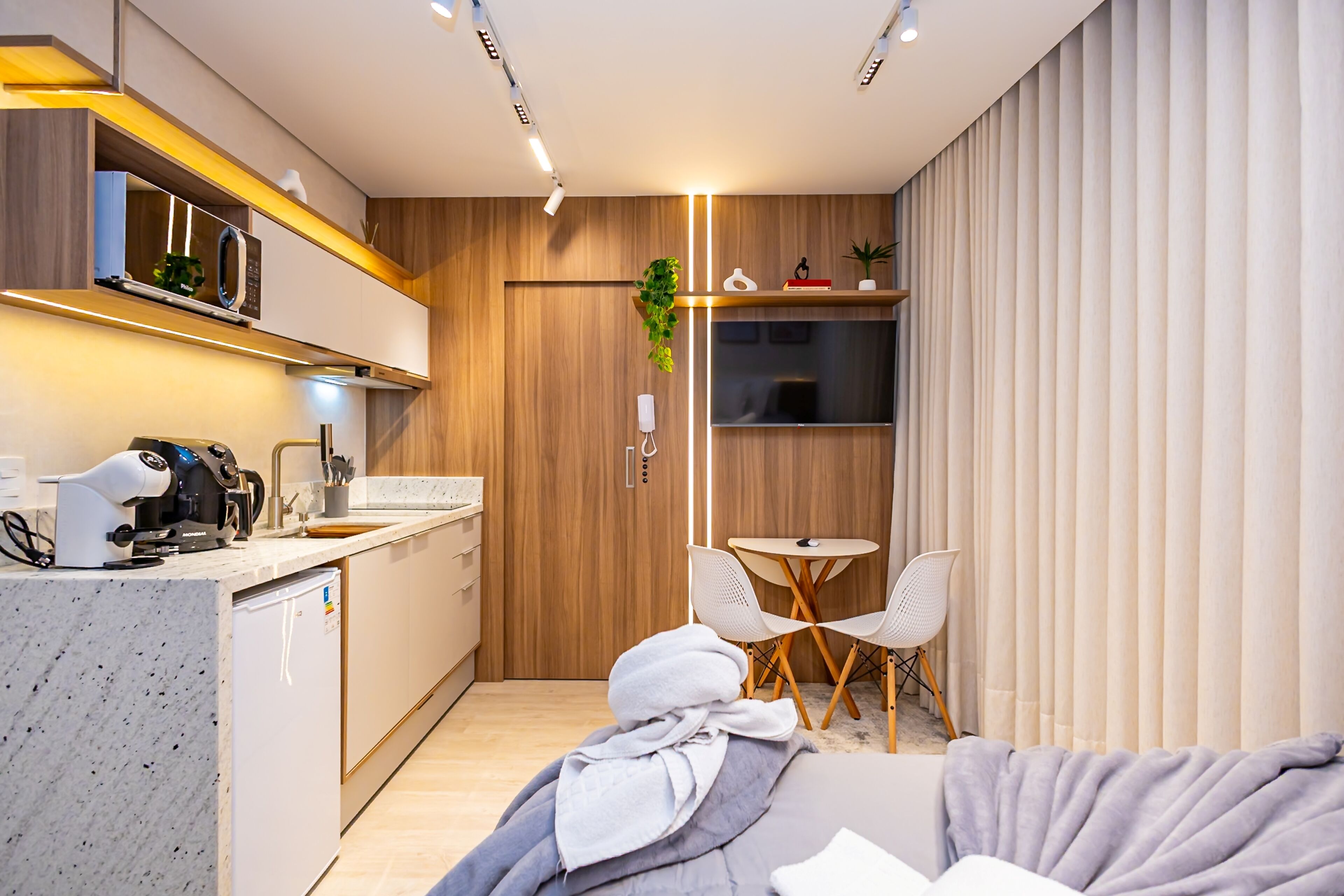 A modern kitchen with a built-in microwave, a coffee machine, and a small refrigerator. There is a dining area with a round table and two chairs.