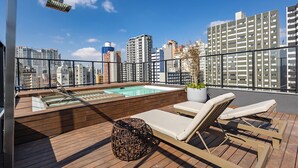 A rooftop pool area with lounge chairs and a hot tub, surrounded by city buildings. - Oxygen Batel (Curitiba)