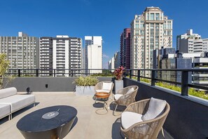 A rooftop terrace with outdoor seating, a potted plant, and a view of surrounding high-rise buildings.