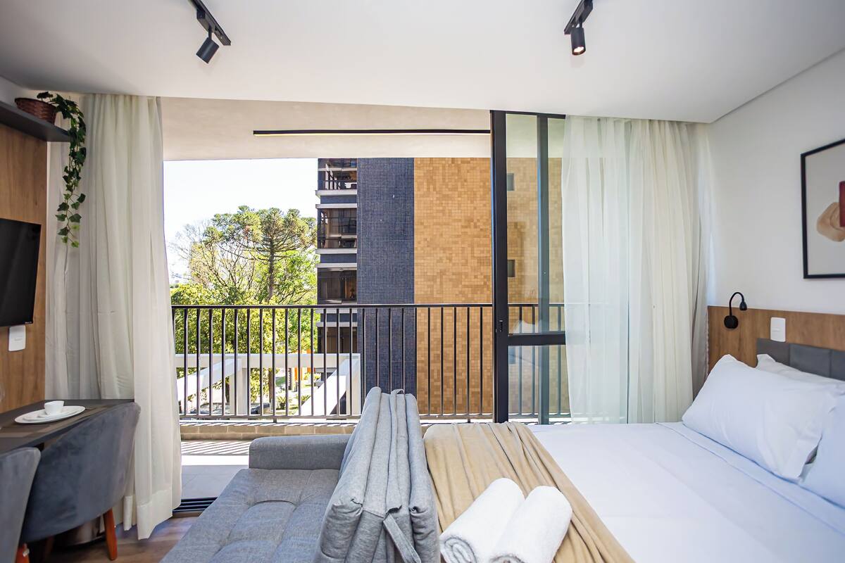 A modern hotel room with a balcony, a sofa, a bed, and a TV.