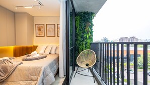A modern bedroom with a bed, a chair, and a balcony with a view of the city. - Oxygen Batel (Curitiba)