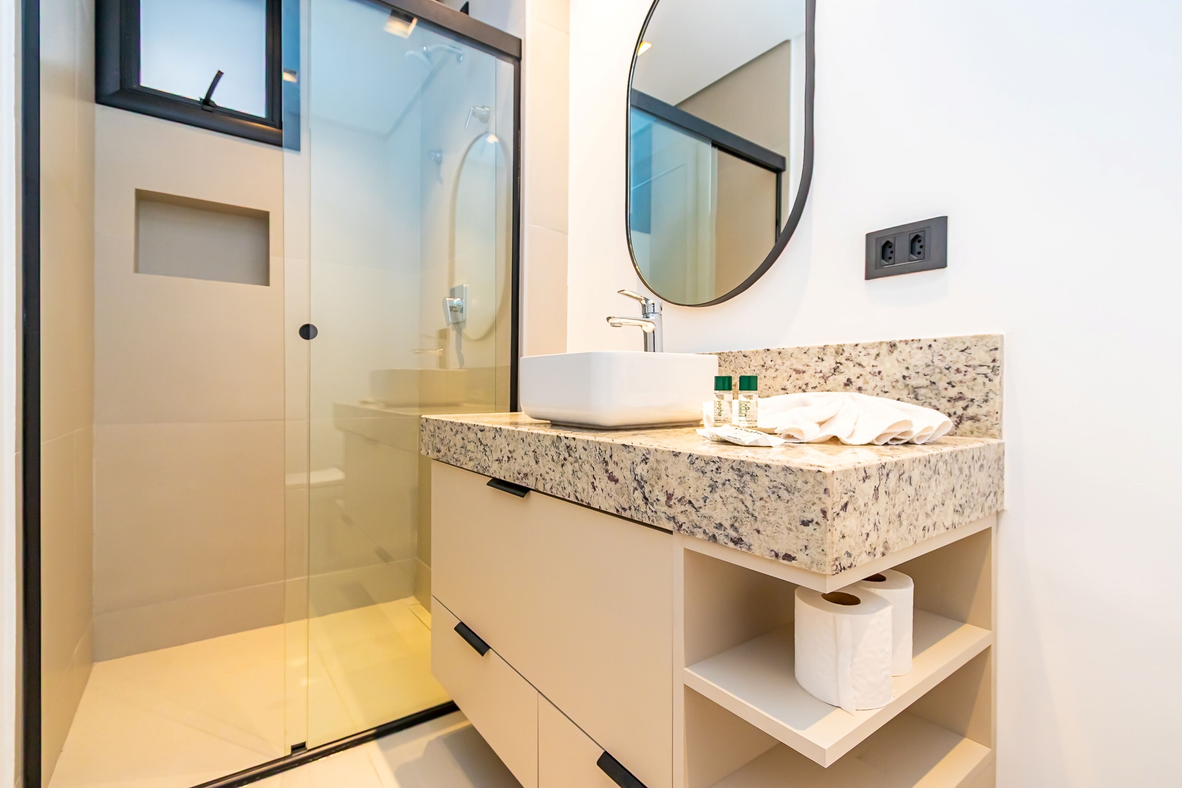 Une salle de bain moderne avec une douche à parois de verre, un lavabo blanc doté d’un plan de travail en granit et un miroir au-dessus du lavabo.