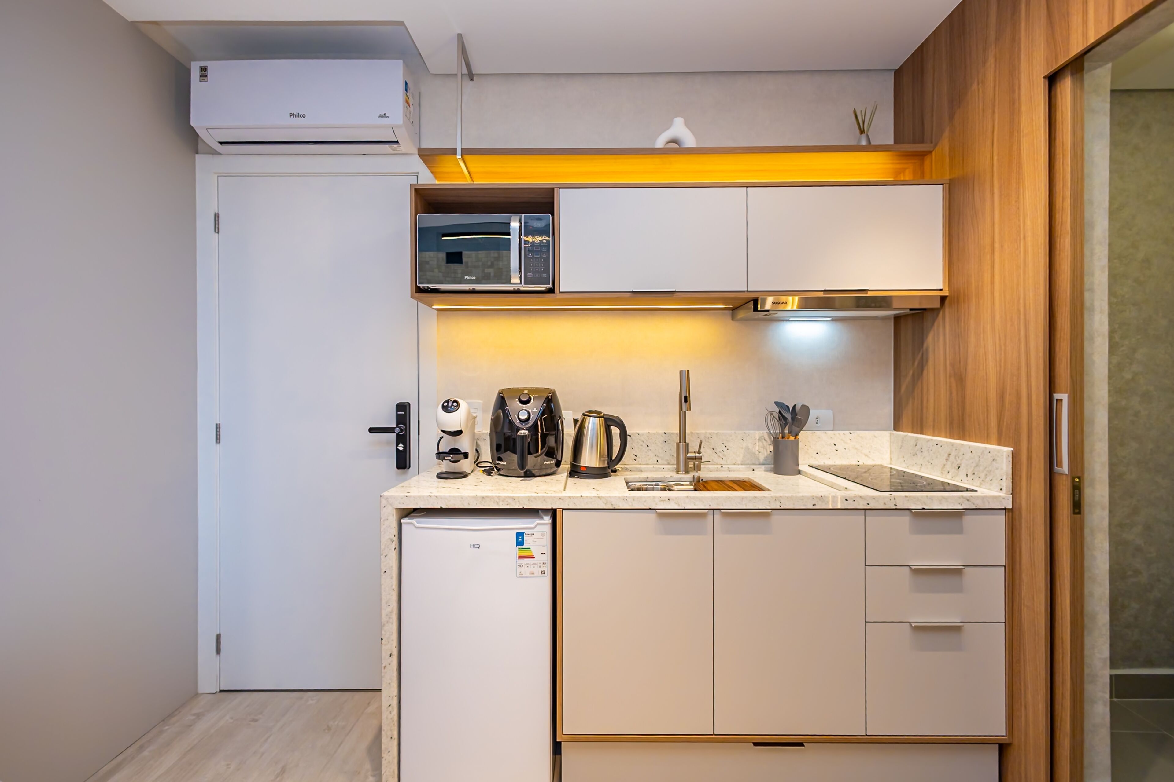A compact kitchen with a microwave, coffee maker, kettle, and a small refrigerator.