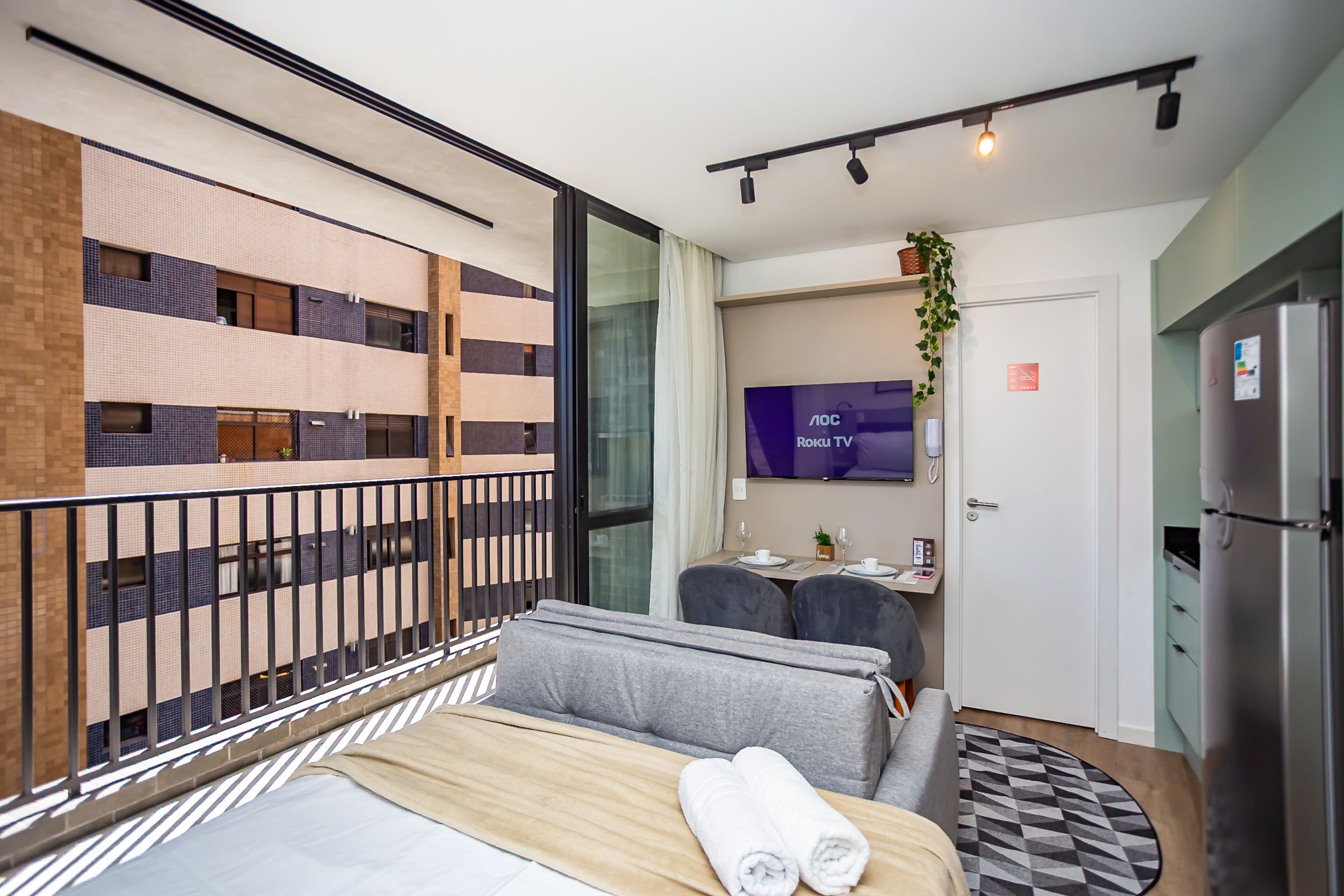 Una habitación de hotel con cama, escritorio, silla, televisor y refrigerador.