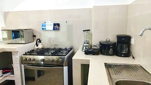 Una cocina compacta equipada con estufa a gas, microondas, cafetera y hervidor.