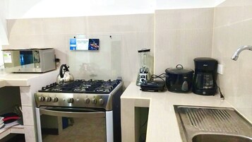 Una cocina compacta equipada con estufa a gas, microondas, cafetera y hervidor.