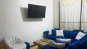 Una sala de estar con un sofá azul, un sillón gris, una mesa de centro y un televisor de pantalla plana montado en la pared.