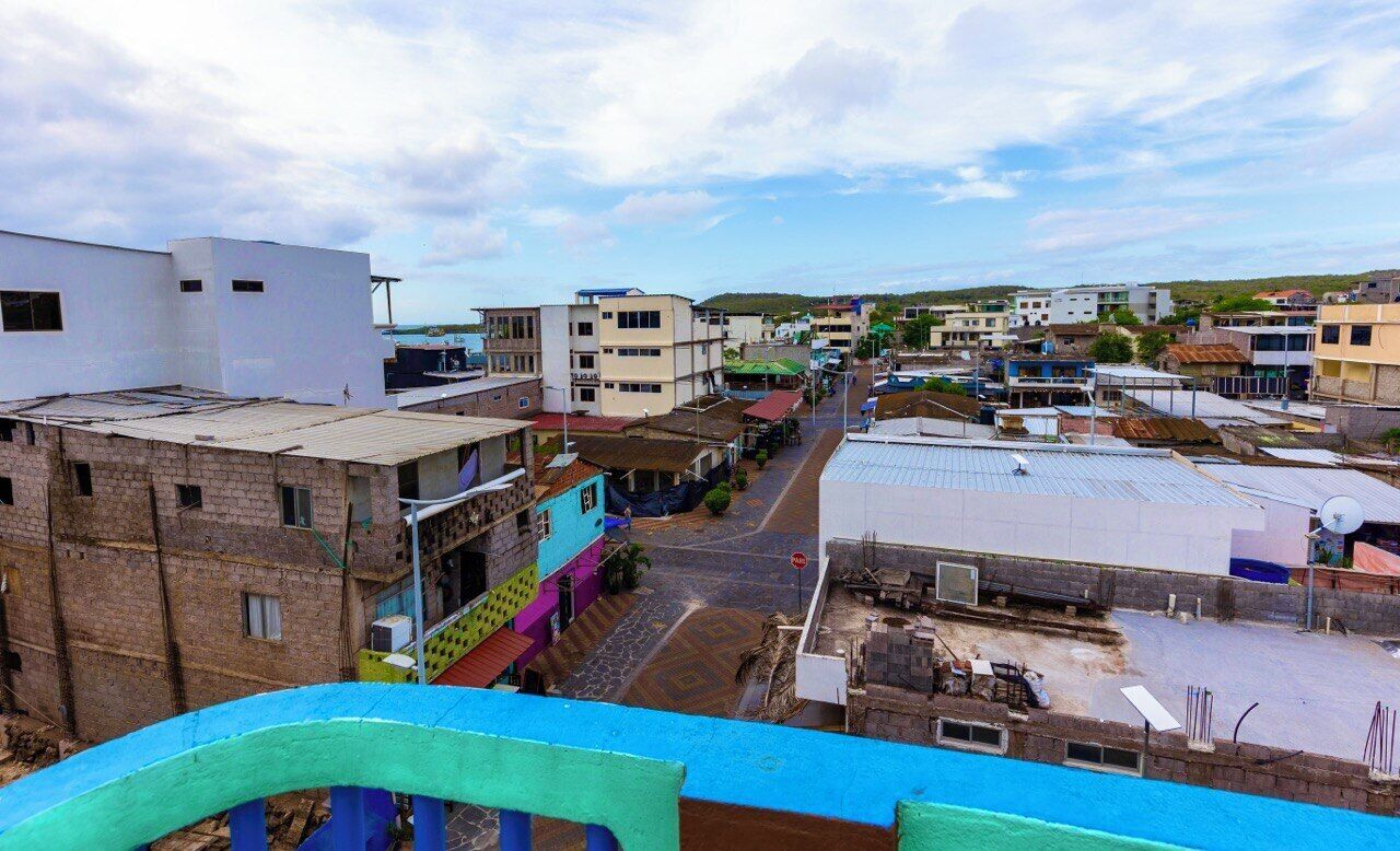 Una vista de carrer d'una població amb edificis de diverses mides i colors, incloent-hi un edifici blanc destacat amb teulat pla i un edifici amb teulat a dos vessants de colors.