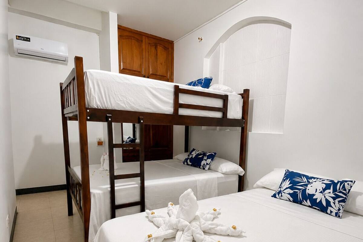 Habitación con literas, aire acondicionado blanco, cabecero de madera y una decoración de toalla con forma de estrella.
