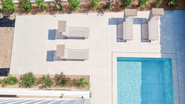 Vista aerea di una zona piscina con quattro lettini e un solarium bianco.