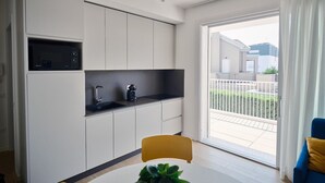 Una cucina moderna con forno a microonde integrato, macchina del caffè e lavello. C'è una zona pranzo con tavolo e sedie, e un'ampia porta-finestra scorrevole che dà su un balcone.