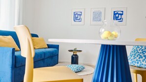 Un soggiorno moderno con un divano blu, poltrone gialle, un tavolino da caffè bianco con una gonna blu e tre opere d'arte incorniciate appese al muro.