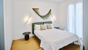 Una camera da letto con una testiera imbottita verde, una coperta bianca, un'amaca sospesa e un tavolino rotondo con un vaso.