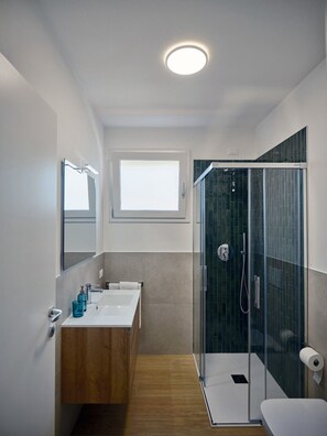 Un baño moderno con cabina de ducha de vidrio, tocador de madera, espejo grande y ventana sobre el lavabo.