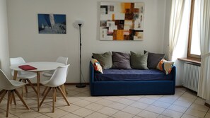 Un saló amb un sofà blau, cadires blanques, una taula, un quadre i una làmpada de peu.
