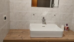 Un baño con lavamanos blanco, encimera de madera y paredes con azulejos.