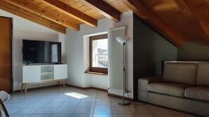 Una sala de estar con un televisor sobre un mueble bajo, un sofá, un radiador y una ventana con vistas.