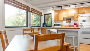 Una cocina moderna con armarios de madera, encimera blanca y un comedor con mesa y sillas de madera.