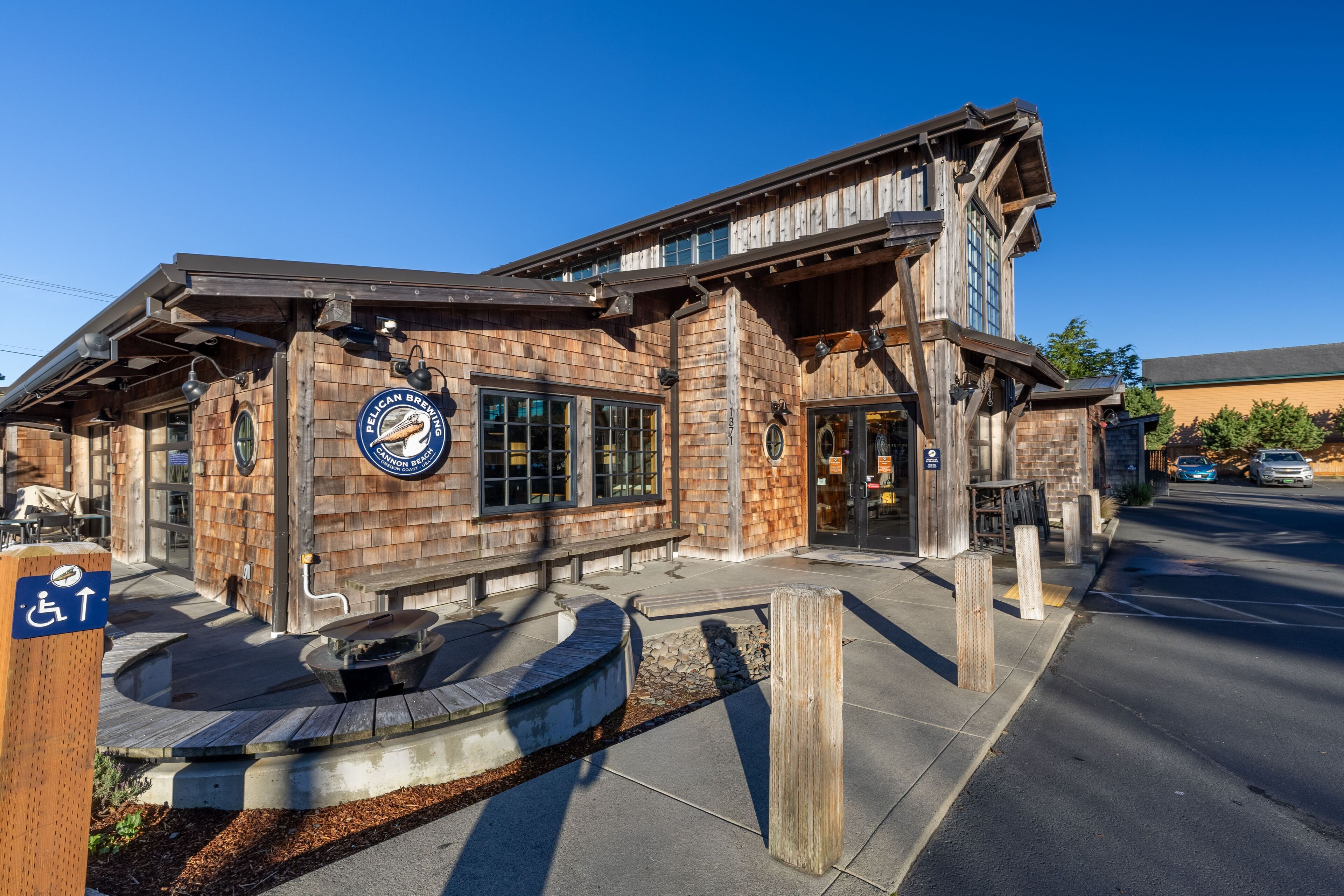 Un bâtiment doté d’une façade en bois rustique, une enseigne indiquant la présence d’un restaurant et un panneau signalant l’accessibilité aux personnes à mobilité réduite.
