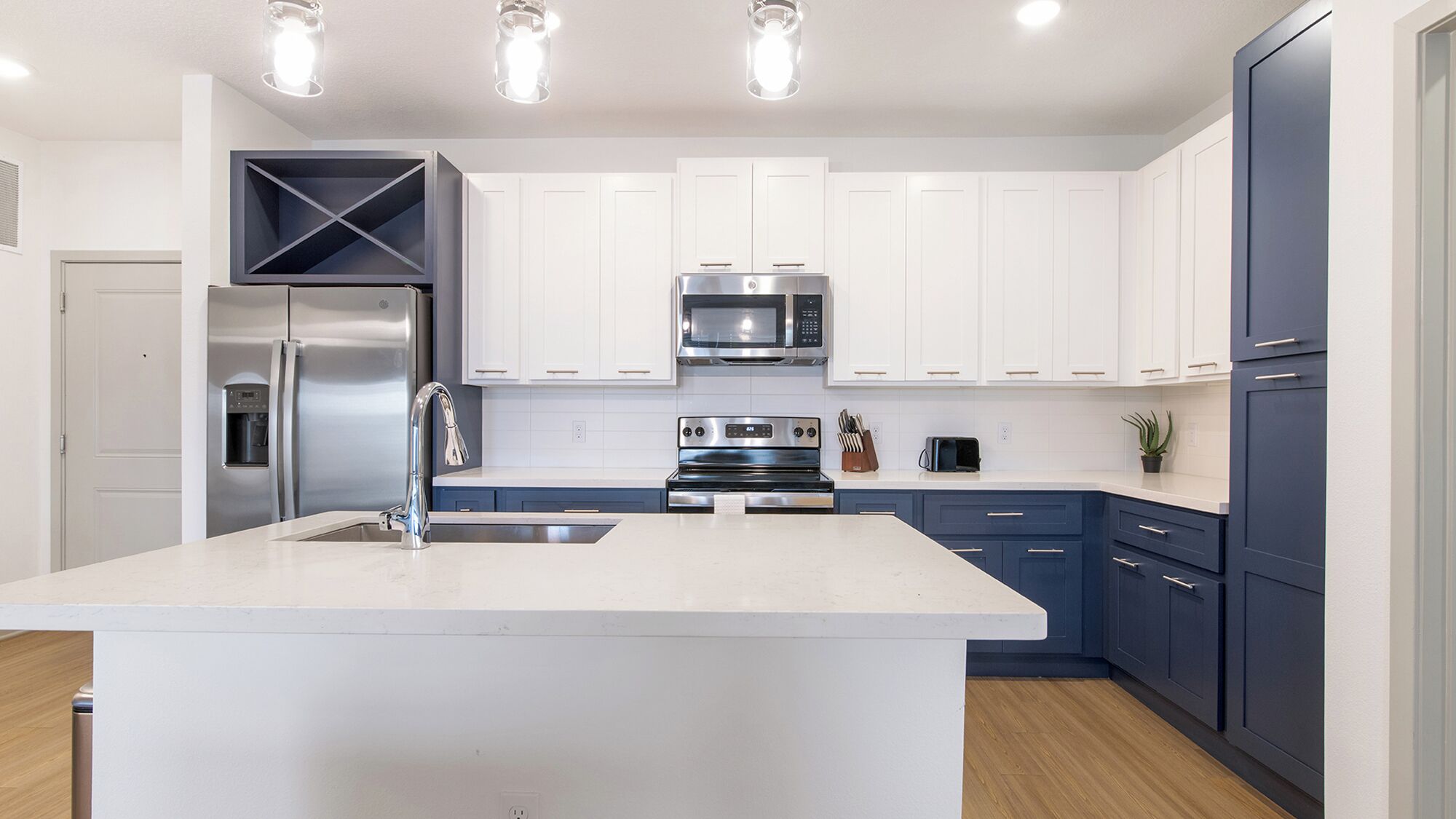A modern kitchen with white cabinets, a stainless steel refrigerator, a microwave, an oven, and a sink.
