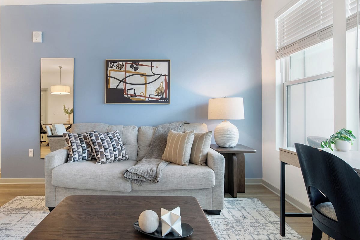 Sala de estar com sofá cinza, mesa de centro com objetos decorativos, luminária e janela com persianas.