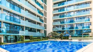 A modern hotel with a large indoor swimming pool, multiple balconies, and a well-maintained garden area. - Stayshort - 1 Bed in Business Bay That Sleeps 4 Perfect for Everyone (Dubai)