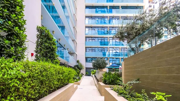 A modern building with a central walkway flanked by greenery and a low wall. - Stayshort - 1 Bed in Business Bay That Sleeps 4 Perfect for Everyone (Dubai)