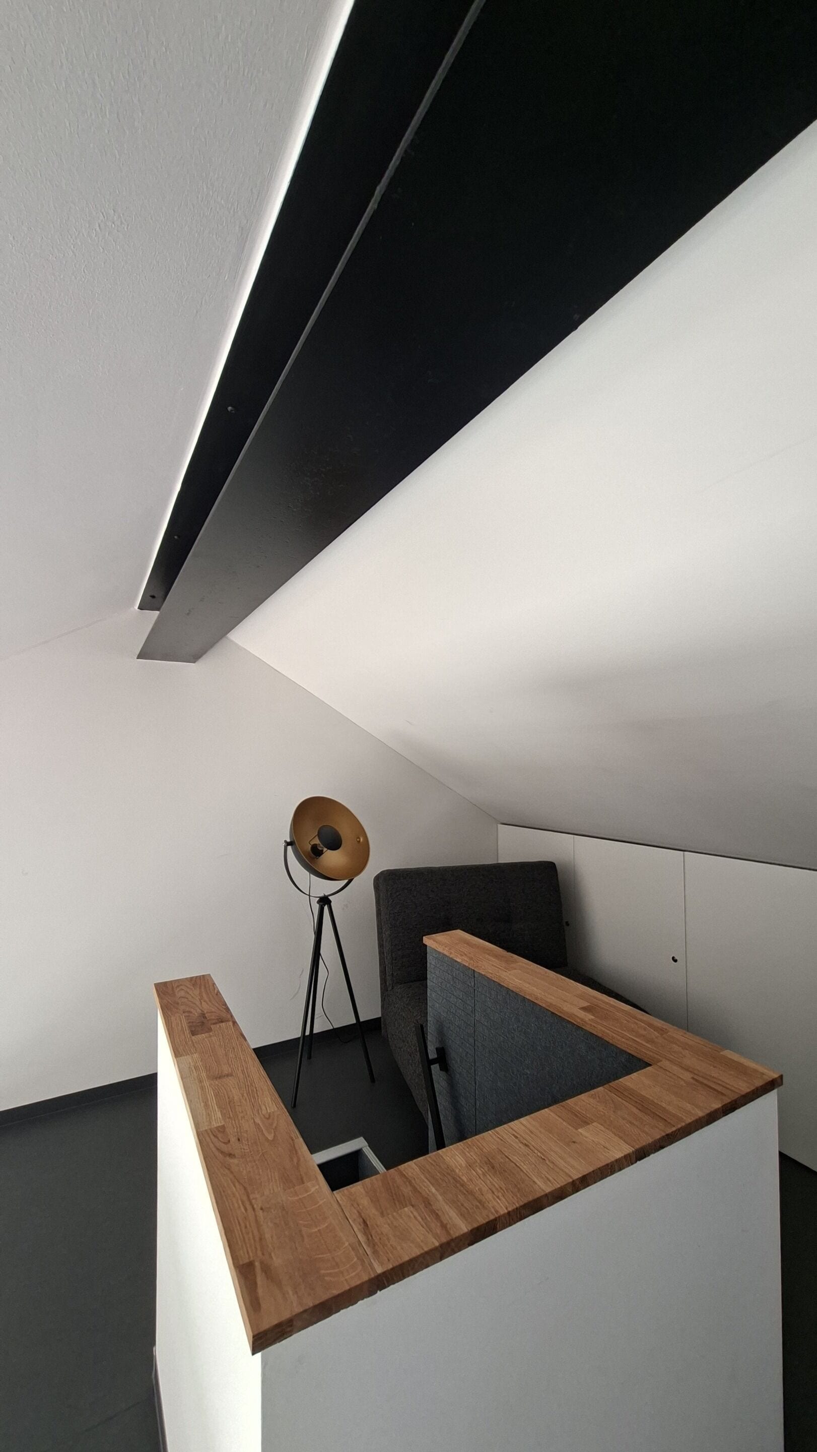 Ein moderner, minimalistischer Raum mit schrägem Dach, einer Holzvertäfelung, einem grauen Sofa und einer Stehlampe.