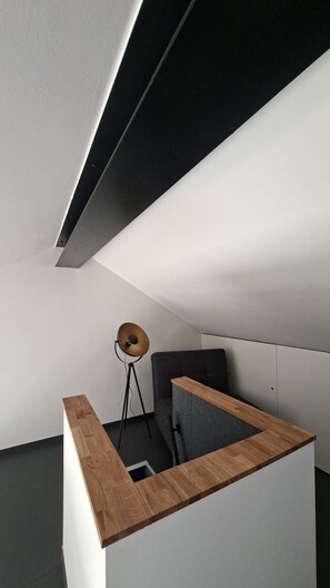 A modern, minimalist room with a sloped ceiling, a wooden accent wall, a grey sofa, and a floor lamp. - SMART LODGES (Bad Rippoldsau-Schapbach)